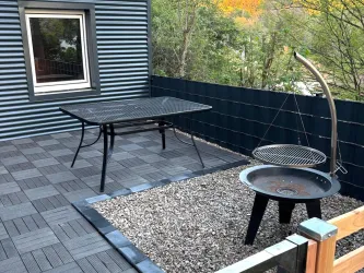 Eine Terrasse mit einem Tisch und einem Grill. Der Boden ist mit Platten und Kies gestaltet.