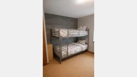 Ein Etagenbett mit zwei Matratzen in einem hellen Raum. Der Boden ist beige und die Wände sind schlicht gestaltet.