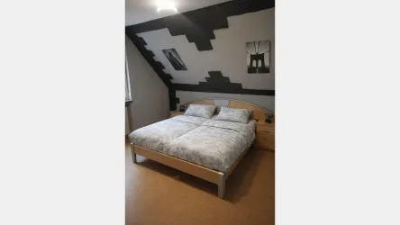 Ein modernes Schlafzimmer mit einem großen Bett und einer hellen Bettwäsche. Die Wände sind in neutralen Farben gestaltet und es gibt einige einfache Bilder im Raum.