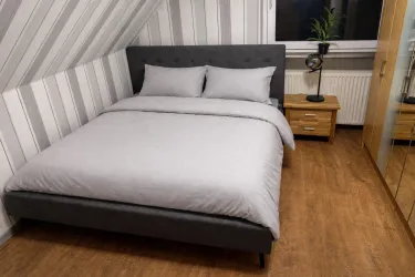 Ein gemütliches Schlafzimmer mit einem grauen Bett und weichen Kissen. Die Wände sind gestreift und ein Holzmöbelstück ergänzt den Raum.