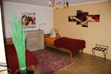 Ein gemütliches Zimmer mit zwei Betten und einem bunten Teppich. An der Wand hängen moderne Bilder und eine Lampe sorgt für Licht.