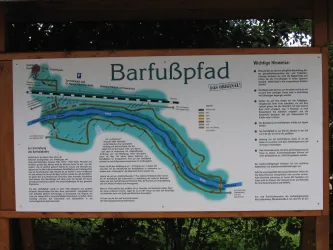 Ein Informationsschild zum Barfußpfad, das den Verlauf und die Details des Weges zeigt. Es enthält Karten und Hinweise für Besucher.