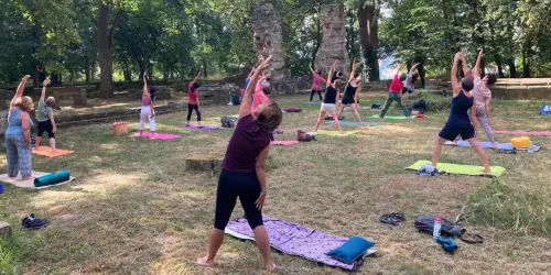 Eine Gruppe von Menschen macht Yoga im Freien auf bunten Matten. Die Umgebung ist grün und herzlichen, ideal für Entspannung und Bewegung.