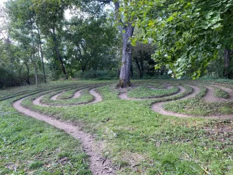 Ein kreativer Bodenlabyrinth in einem Park, umgeben von Bäumen. Der Weg ist sanft geschwungen und lädt zum Entdecken ein.