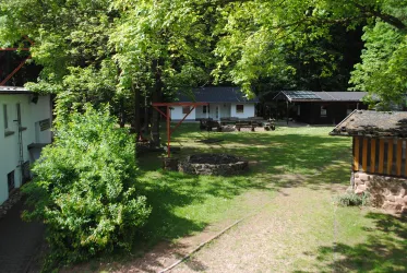 Eine ruhige Gartenlandschaft umgeben von Bäumen. Im Hintergrund sind verschiedene Gebäude zu sehen.