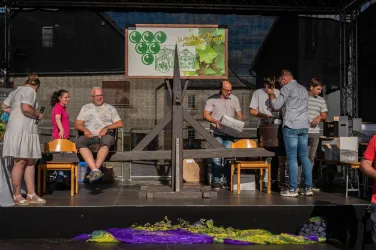 Eine Veranstaltung mit Menschen, die an einem Tisch arbeiten. Im Hintergrund sind Weinfässer und ein Schild mit Weinmotiven zu sehen.
