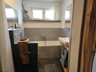 Ein modernes Badezimmer mit einer Badewanne und einem Waschbecken. Es ist hell und einladend, mit Holzdetails und neutralen Farben.