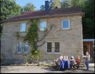 Ein stilvolles Haus aus Stein mit einer aufwachsenden Pflanze an der Wand. Eine Gruppe älterer Menschen sitzt entspannt an einem Tisch im Freien.