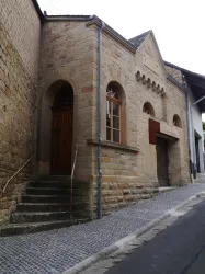 Ein historisches Gebäude mit einer steinernen Fassade und großen Fenstern. Die Treppe führt zu einem Holzportal.