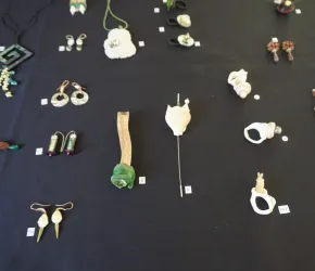 Eine Auswahl an Schmuckstücken liegt auf einem schwarzen Tisch. Die Stücke bestehen aus verschiedenen Materialien und Formen, darunter Ohrringe und Broschen.