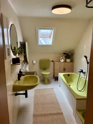 Ein modernes Badezimmer mit gelben Sanitäranlagen und einer Badewanne. Große Fenster sorgen für natürliches Licht und eine angenehme Atmosphäre.