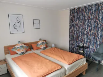 Ein gemütliches Schlafzimmer mit einem Doppelbett und orangefarbenen Decken. Die Wände sind mit einem dekorativen Muster und einem Kunstwerk geschmückt.