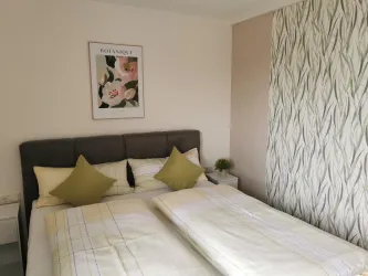 Ein modernes Schlafzimmer mit einem Doppelbett und zwei Kissen. An der Wand hängt ein dekoratives Bild und die Tapete hat ein elegantes Muster.