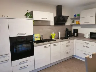 Moderne Küche mit hellen Holzoberflächen und einer dunklen Arbeitsplatte. Es gibt einen Herd, eine Kaffeemaschine und verschiedene Küchenutensilien.