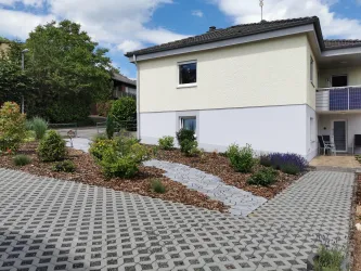 Ein modernes Haus mit einem gepflegten Garten. Der Weg ist mit Steinen gepflastert und es gibt viele Pflanzen rund um das Haus.