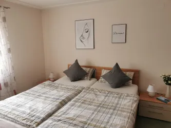Ein gemütliches Schlafzimmer mit zwei Einzelbetten und dekorativen Kissen. An der Wand hängen zwei gerahmte Bilder, und ein kleiner Blumenstrauß steht auf dem Nachttisch.