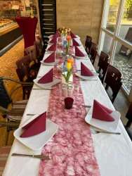 Ein festlich gedeckter Tisch mit weißen Tellern und roten Servietten. In der Mitte stehen Blumenvasen mit bunten Tulpen.