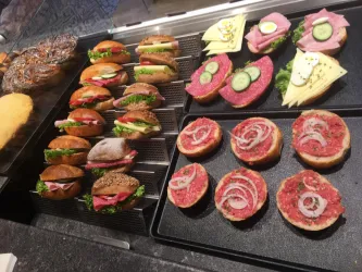 Eine Auswahl an belegten Brötchen mit frischem Gemüse und verschiedenen Aufschnittsorten. Dazu gibt es spezielle Häppchen mit Fleisch und Käse auf einem Teller.