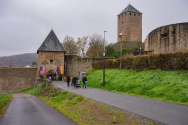 Ein historisches Schloss mit Türmen und einer Steinmauer. Besucher gehen den Weg entlang, um das Schloss zu erkunden.