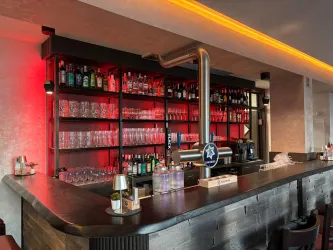 Ein Blick auf die Bar des Visà Vis mit gut gefüllten Regalen und einer eleganten Theke. Die Beleuchtung schafft eine einladende Atmosphäre.