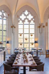 Ein eleganter Restaurantbereich mit hohen, gotischen Fenstern. Der Tisch ist schön gedeckt und mit Blumen dekoriert.