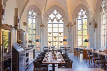 Ein elegantes Restaurant mit hohen, gitterverzierten Fenstern. Die Tische sind liebevoll gedeckt und bieten einen Blick auf die grüne Umgebung.