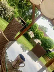 Ein schöner Garten mit einem Tisch aus Glas und einem Becher. Im Hintergrund sind stilvolle Gartenmöbel und üppige grüne Pflanzen zu sehen.