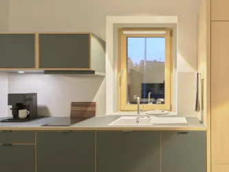 Eine moderne Küche mit grünen Schränken und einem Fenster, das Tageslicht hereinfällt. Auf der Arbeitsplatte steht eine Kaffeemaschine und ein paar Küchenutensilien.