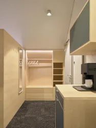 Ein modernes Zimmer mit Holzregalen und einem Spiegel. Auf einem Tisch steht eine Kaffeemaschine und eine Tasse.