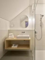 Ein modernes Badezimmer mit einer Glasdusche und einem Holzwaschtisch. Handtücher sind ordentlich gestapelt und es gibt eine runde Spiegelbeleuchtung.
