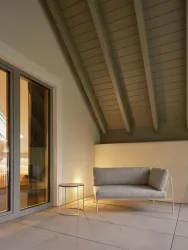 Eine gemütliche Terrasse mit einem grauen Sofa und einem kleinen Tisch. Der Raum hat hohe Decken und große Fenster, die viel Licht hereinlassen.