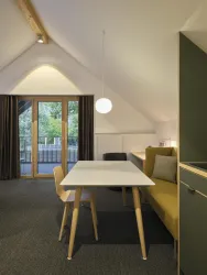 Ein modernes Zimmer mit einem weißen Tisch und Stühlen. Große Fenster bieten einen Blick nach draußen und sorgen für viel Tageslicht.