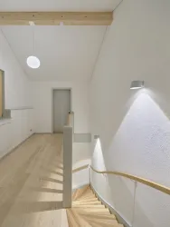 Ein helles Treppenhaus mit Holztreppe und minimalistischer Beleuchtung. Die Wände sind weiß, und es gibt eine harmonische Atmosphäre.