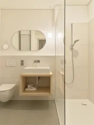 Eine moderne Badezimmeransicht mit einem klaren Duschbereich und einem Waschbecken aus Holz. Die Wände sind in neutralen Farbtönen gehalten und das Licht ist angenehm.