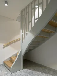 Eine moderne Wendeltreppe aus Holz und Metall. Der Raum ist hell und schlicht gestaltet.