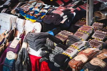 Ein bunter Stand mit einer Vielzahl von Socken und Handschuhen. Die Produkte sind ordentlich gestapelt und zum Verkauf angeboten.