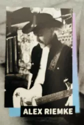 Ein Musiker spielt Gitarre und trägt einen Cowboyhut. Die Szene hat eine lebendige Atmosphäre mit einer unscharfen Hintergrundbeleuchtung.