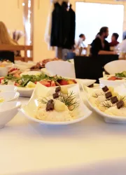 Ein festlich gedeckter Tisch mit mehreren Tellern, die verschiedene Gerichte präsentieren. Im Vordergrund sind Schalen mit Reis, Kräutern und kleinen Fleischstücken sichtbar.