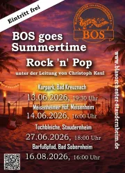 Eine große Gruppe von Musikern steht im Freien und lächelt. Sie tragen schwarze Kleidung mit orangefarbenen Akzenten und halten verschiedene Musikinstrumente.