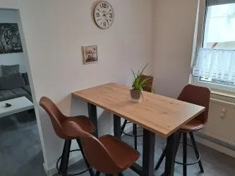 Ein moderner Essbereich mit einem Holztisch und vier Stühlen. Auf dem Tisch steht eine Pflanze und an der Wand hängt eine Uhr.