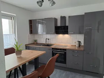 Eine moderne Küche mit grauen Möbeln und einer Holzarbeitsfläche. Ein Esstisch mit zwei Stühlen steht in der Mitte des Raumes.