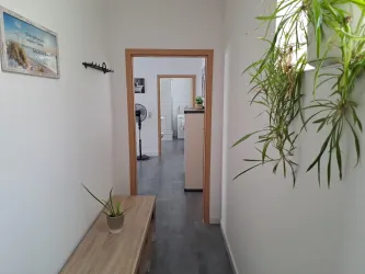 Ein heller Flur mit einem Holztisch und einer Pflanze. Im Hintergrund sind weitere Räume sichtbar.