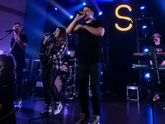 Auftrittsfoto der Liveband Shakers  während die Lichter blitzen. Die MusikerInnen zeigen ihre Energie und begeistern das Publikum.