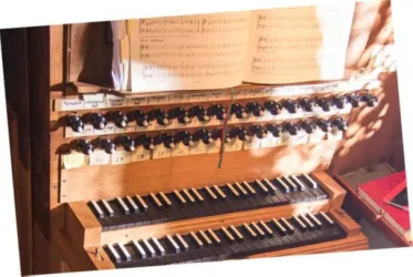 Eine Orgel mit schwarzen und weißen Tasten sowie mehreren Reglern. Im Hintergrund liegt ein offenes Notenbuch.