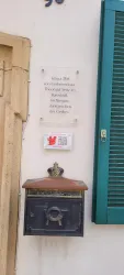 Historische Informationstafel am Eingang. Neben dem Briefkasten befindet sich ein QR-Code.