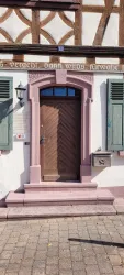 Eine schöne Eingangstür mit einem holzernen Design und einem rosa Rahmen. Die Fassade des Hauses ist mit klassischen Fensterläden geschmückt.