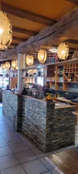 Eine gemütliche Bar mit einer Steintheke und warmen Holzdetails. Über der Theke hängen stilvolle Lampen, die eine einladende Atmosphäre schaffen.