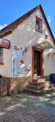 Ein kleines Restaurant mit einem einladenden Eingang. An der Fassade hängen Speisekarten und das Logo des Lokals.