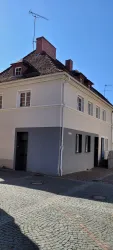 Ein zweigeschossiges Haus mit einer hellen Fassade und einem schrägen Dach, das Gebäude befindet sich an einer ruhigen Straße.