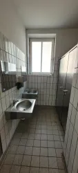 Innenbereich der öffentlichen Toiletten. Es gibt ein Fenster, das Tageslicht hereinlässt.